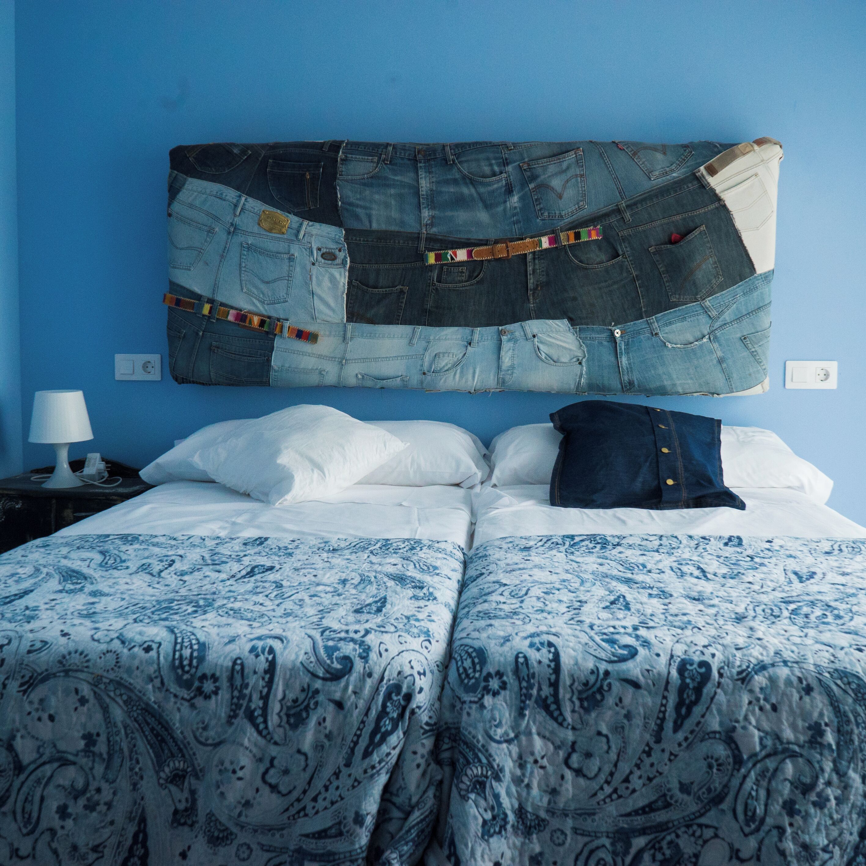 En seng med et blåt og hvidt mønstret sengetæppe, en denim-hovedgærde og hvide puder.