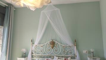 A bedroom with a bed under a white canopy, a nightstand with a lamp, and a wall socket.