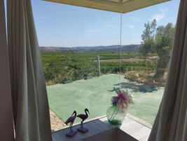 Vista desde una habitación con un ventanal grande que da a un paisaje verde con árboles y colinas distantes.