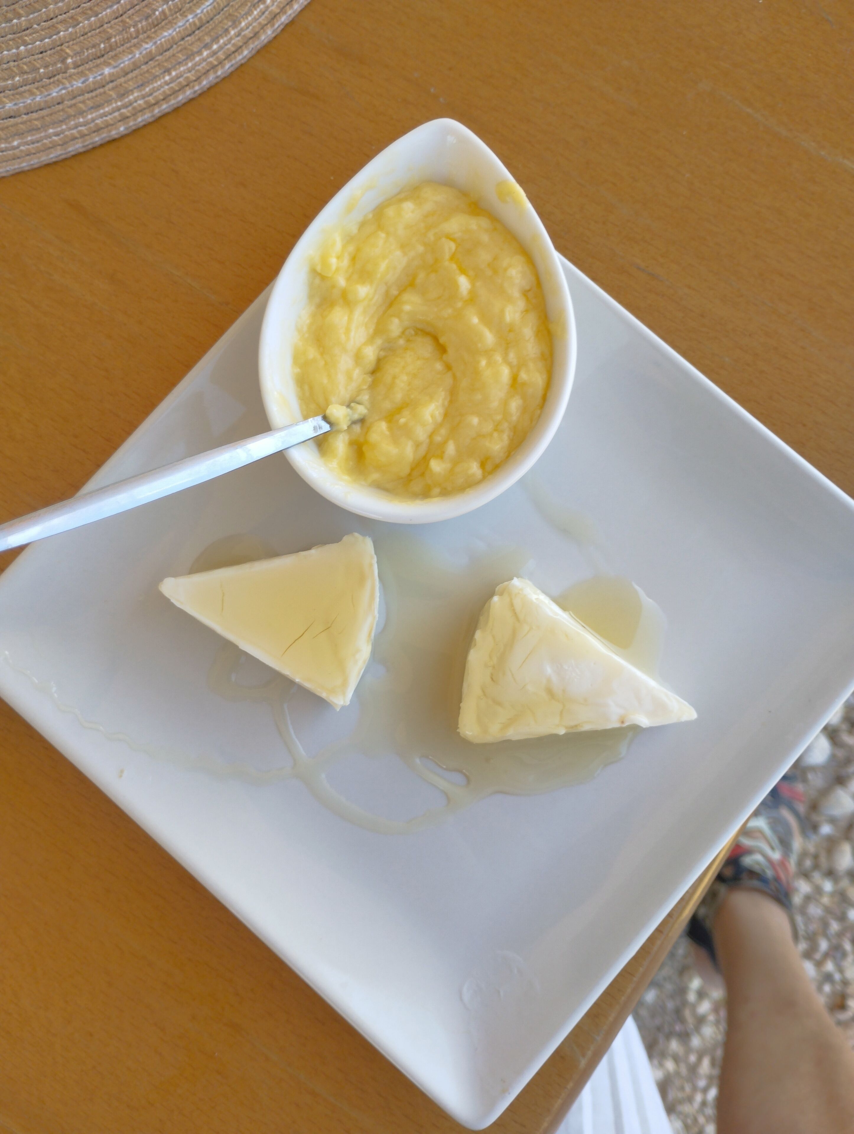 Un plato blanco con un cuenco de salsa amarilla y dos porciones triangulares de comida sobre una mesa de madera.