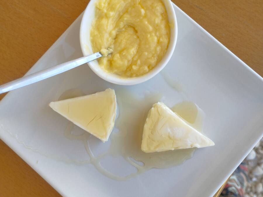 Un plato blanco con un cuenco de salsa amarilla y dos porciones triangulares de comida sobre una mesa de madera.