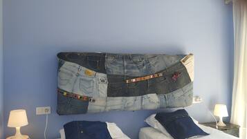 Een kamer met twee bedden, een wanddecoratie van denim en een nachtkastje met een lamp.