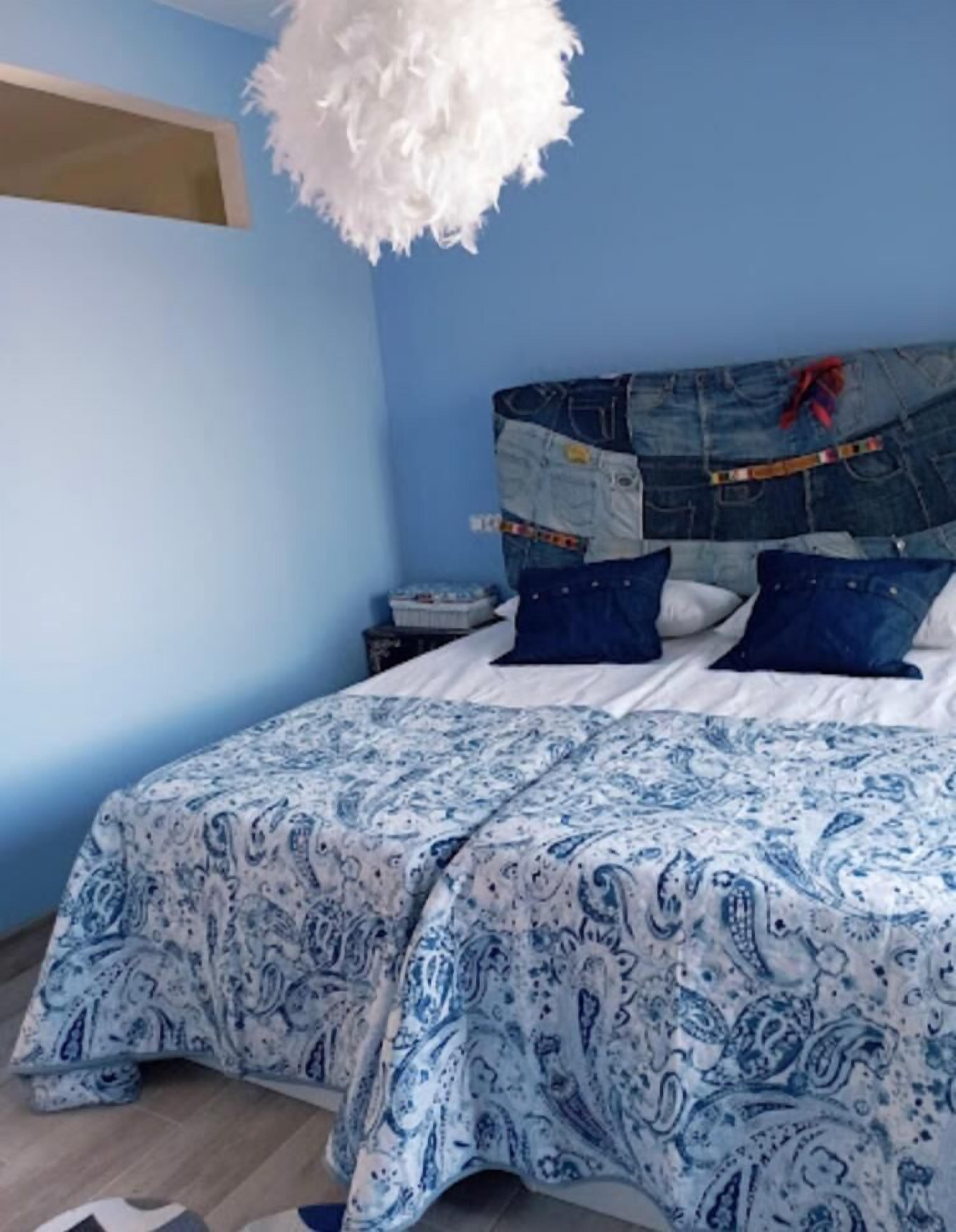 Un dormitorio con colcha estampada azul y blanca, una lámpara colgante blanca y esponjosa, y cabecera de tela vaquera.