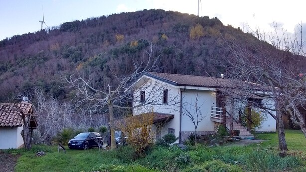 Una casa con techo inclinado, un pequeño jardín y un coche estacionado en la entrada.
