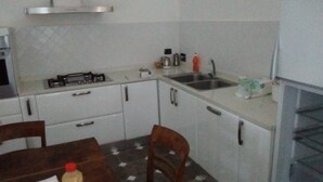 Una cocina compacta con armarios blancos, estufa a gas, lavamanos y comedor con mesa y sillas.