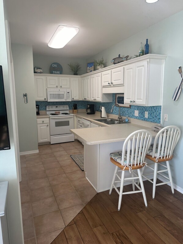 A kitchen with white cabinets, a central island with two bar stools, a microwave, a stove, and a sink.