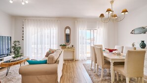 A modern living room with a sofa, TV, and dining area with chairs and a table. - Casa da Praia with pool area
 (Porches)