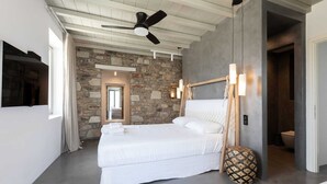 Een moderne slaapkamer met een stenen muur, een plafondventilator, een bed met witte beddengoed en een kamerkleed met patroon.