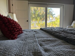 Relax in this serene bedroom with a large bed, sliding glass door to a lush outdoor area, and a comfortable chair.