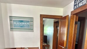Ein Speisebereich im Strandhausstil mit einem Tisch für zwei Personen, einer Bank und einem Wandschild mit der Aufschrift 'BEACH HOUSE'.