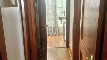 A hallway with wooden flooring leading to a bathroom with a shower and a sink.