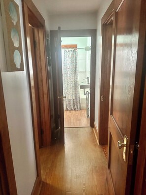 A hallway with wooden flooring leading to a bathroom with a shower and a sink.