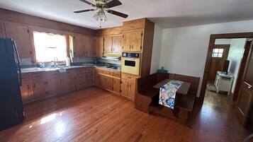 Una cocina con armarios de madera, una estufa, un ventilador de techo y un comedor con mesa.