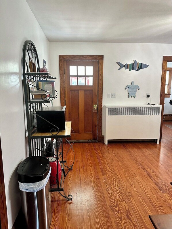 A room with a wooden floor, a white radiator, a wooden door, and a metal shelf with books and a red kettle. - ESVA Down by the Sea & Pet Friendly (Onancock)