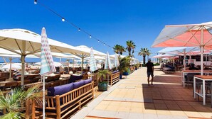 An outdoor dining area with wooden benches and tables, surrounded by umbrellas and potted plants. - Ramat Yam Marine - Two Bedroom Apartment, Sleeps 4 (Tel Aviv-Yafo)