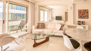 A modern living room with a glass coffee table, white sofa, and a dining area with a marble table. - Ramat Yam Marine - Two Bedroom Apartment, Sleeps 4 (Tel Aviv-Yafo)