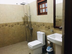 Et badeværelse med toilet, vask, brusebad og et vindue.