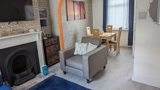 A living room with a fireplace, a sofa, a dining table with chairs, and a TV mounted on the wall. - Fantastic Location to Ebrington Sq and City Centre (Londonderry)