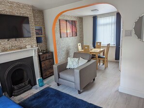 Una sala de estar con chimenea, un sofá, una mesa de comedor con sillas y un televisor montado en la pared.