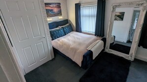 A bedroom with a bed, a large mirror, a window with curtains, and a brick wall. - Fantastic Location to Ebrington Sq and City Centre (Londonderry)