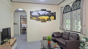 A living room with a sofa, a coffee table with plants, a TV, and a painting on the wall. - Getaway near Patong Beach, shops and restaurants. Homey, private, and memorable. (Tambon Patong)