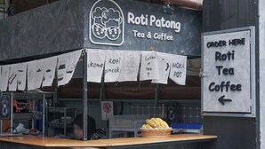 A Roti Patong Tea & Coffee stall with a signboard, a display of bananas, and a counter with a basket of bananas. - Getaway near Patong Beach, shops and restaurants. Homey, private, and memorable. (Tambon Patong)