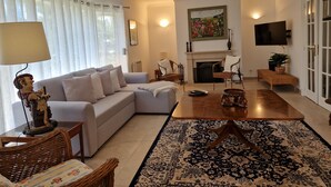 A living room with a sofa, chairs, a coffee table, a fireplace, a TV, and a large window with curtains.
