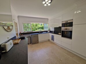 Eine moderne Küche mit weißen Schränken, einem eingebauten Backofen, einem Geschirrspüler und einem Fenster mit Blick auf Grünflächen.