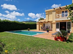 A two-story house with a swimming pool, patio furniture, and potted plants.