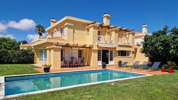 A two-story house with a swimming pool, outdoor seating, and a well-maintained lawn.