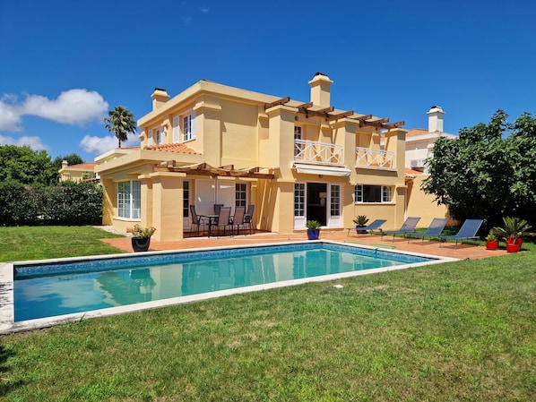 Ein zweistöckiges Haus mit Pool, Sitzgelegenheiten im Freien und einem gepflegten Rasen.