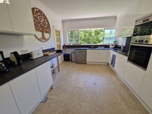 A modern kitchen with white cabinets, a black countertop, a built-in oven, and a window with a view of greenery.