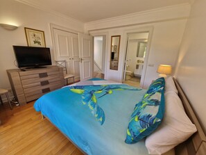 A bedroom with a bed, dresser, television, and a bathroom visible through an open door.
