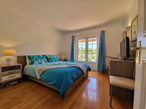 A bedroom with a bed, bedside tables, a desk with a computer, and a window with curtains.