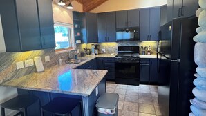 A modern kitchen with dark cabinets, a granite countertop, a stainless steel sink, a black refrigerator, and a stove.