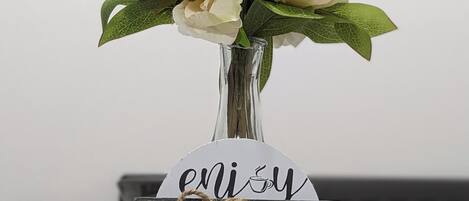 A table with a vase of flowers, a sign with 'enjoy HOME,' and a clock in the background.