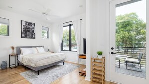 A modern bedroom with a bed, a TV, a balcony with a chair, and large windows.