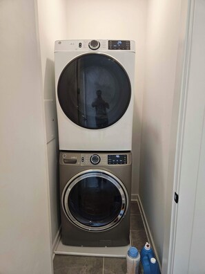 A compact laundry room with a stacked washer and dryer, a tiled floor, and a door leading to another room.