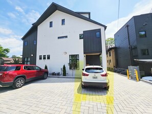 A modern building with a white facade and dark trim, featuring a garage entrance and a paved driveway.