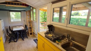 A compact kitchen with a dining table, a sink, and a window overlooking a garden. - La Tiny de Papy (Attignat)