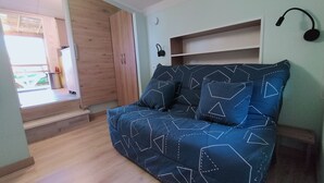 A bedroom with a bed, a wooden wardrobe, a small shelf, and a window with a view of the outside. - La Tiny de Papy (Attignat)