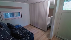 A room with a bed, a window, a curtain, and a door leading to another room. - La Tiny de Papy (Attignat)