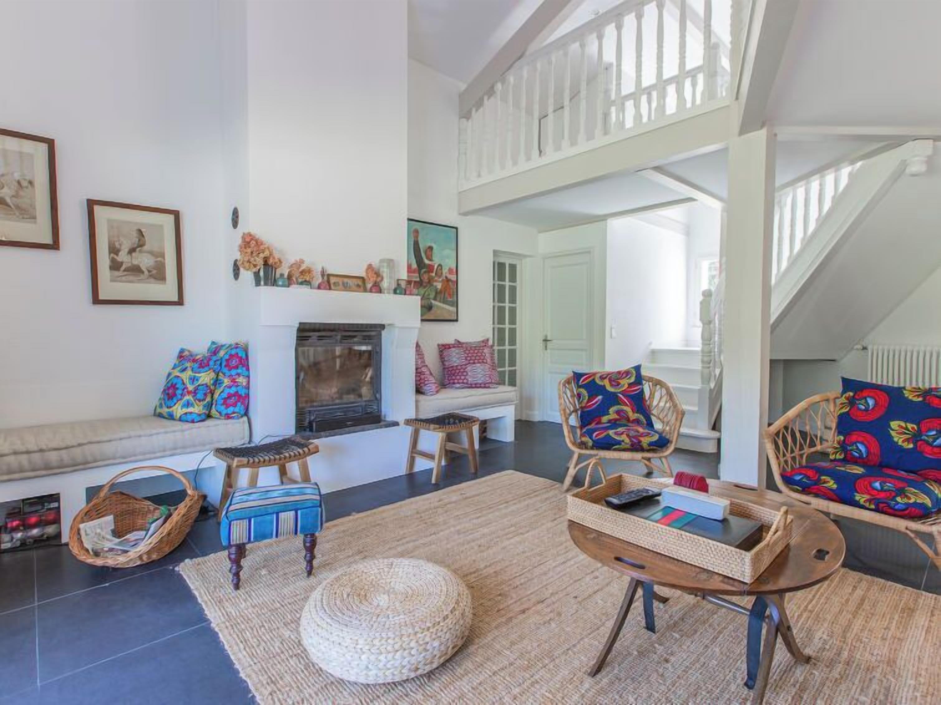 Una sala de estar con chimenea, muebles de mimbre y una escalera.