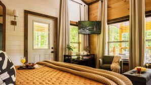 Ein gemütliches Zimmer mit einem großen Bett, einem Flachbildfernseher, einem Schreibtisch mit Stuhl und einem Fenster mit Blick auf Grünflächen.