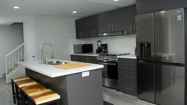 A modern kitchen with a central island, stainless steel appliances, and wooden bar stools. - CASA TOTALMENTE RENOVADA CON TODA LAS COMODIDADES Y CARACTERISTICAS DE ALTA GAMA (Cali)