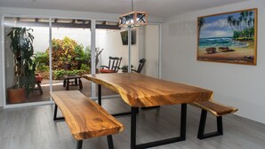 A spacious room with a large wooden dining table, benches, and a view of a tropical outdoor area with plants and a beach scene painting on the wall. - CASA TOTALMENTE RENOVADA CON TODA LAS COMODIDADES Y CARACTERISTICAS DE ALTA GAMA (Cali)