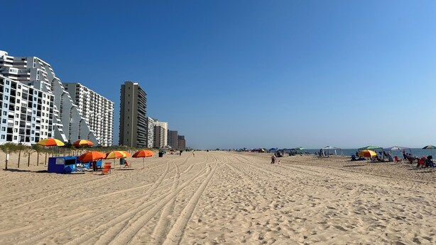 Una playa con una hilera de edificios altos, sombrillas y tumbonas.