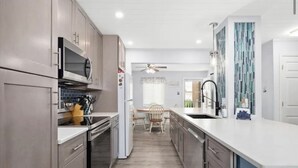 Una cocina moderna con electrodomésticos de acero inoxidable, un comedor con una mesa y sillas de madera, y una pared azul decorativa.