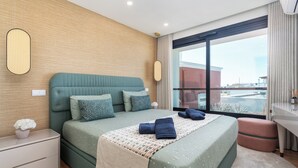 Habitación de hotel moderna con una cama grande, una mesita de noche, una mesita auxiliar pequeña, una ventana con vistas y un área de baño.