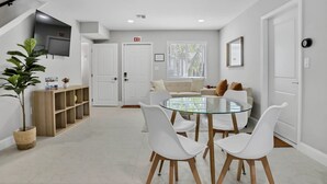 Una sala de estar moderna con una mesa de comedor de vidrio, sillas blancas, un sofá y un televisor montado en la pared.